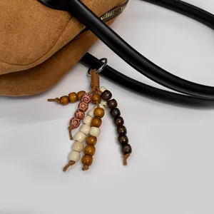 Detail of bohemian wood bead bag charm with brown woven cord on suede handbag
