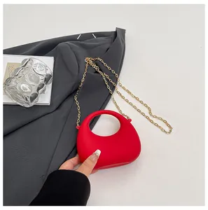 Macro-opname van een rode halve maan tas met gouden ketting op een grijs-witte ondergrond