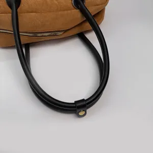 Detail of brown suede handbag featuring black leather handle and gold metal hardware