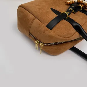 Close-up of brown suede handbag featuring black leather trim and gold metal hardware detail