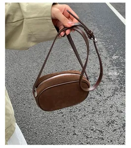 Close-up of brown suede mini round bag with leather trim and adjustable strap detail