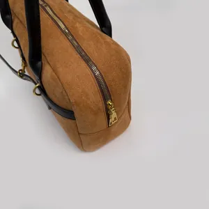 Detail view of brown suede bag with black leather handle and golden zipper hardware