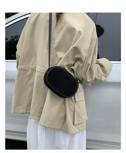 Street style view of a minimalist black suede oval crossbody bag with a slim leather strap
