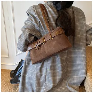 Détail d'un sac porté épaule en daim marron avec boucle dorée et lanière en cuir