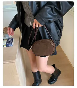 Detail view of brown suede oval crossbody bag with silver zipper and slim leather strap