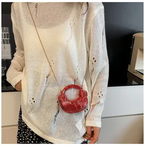 Rote metallische Halbmond-Handtasche mit goldener Kette auf weißem Strick-Outfit