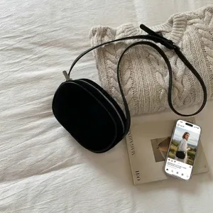 Minimalist black oval crossbody bag in matte suede finish on a soft fabric surface