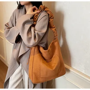 Detail view of brown matte leather shoulder bag with unique pleated strap and front pocket