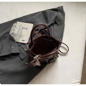 Detail of dark brown leather bucket bag with decorative silk scarf on a gray blazer