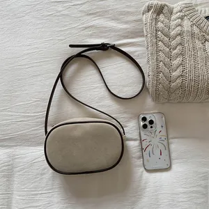 Flat lay of an oval beige crossbody bag with dark brown leather trim on knit fabric