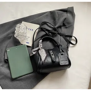 Detail shot of a black bucket bag with silk scarf on handle and leather logo tag