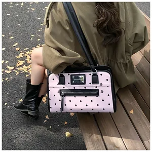Détail du sac à bandoulière rose à pois avec finitions en cuir noir et plaque métal
