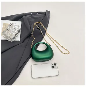 Donkergroene mini handtas met gouden ketting getoond naast een smartphone voor de grootte