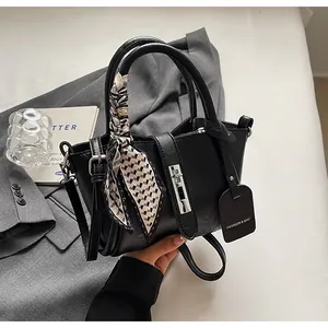 Detail of black leather bucket bag with silver lock and checkered scarf on gray blazer
