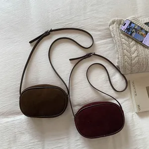 Flat lay of coffee and wine red suede round crossbody bags on a cozy white bedsheet