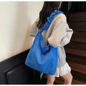 Detail of bright blue tote bag featuring artistic ruched shoulder strap and front pocket