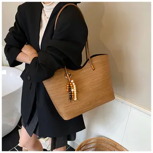 Brown woven tote bag with leather strap and wooden bead charm shown on model shoulder