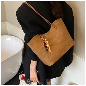 Close-up of brown woven tote bag with wooden bead tassel detail on a female model