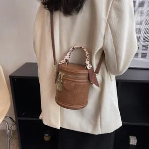 Detail of a retro brown bucket bag with a silk scarf handle and golden padlock charm