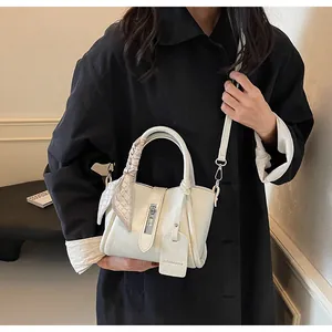 Chic cream bucket bag with silk scarf detail worn with a black coat in a minimalist setting