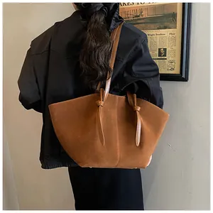 Macro view of brown suede tote bag featuring wing-shaped design and knotted strap details