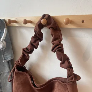 Detail of dark brown faux suede handbag with pleated shoulder strap and metal zipper