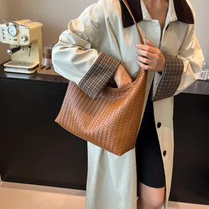 Close-up of a brown woven leather tote bag worn by a model in a cozy cafe setting