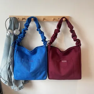 Detail of blue and burgundy matte tote bags with pleated straps on wooden hangers