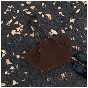Detail of dark brown suede tote bag with knotted handle on autumn leaves