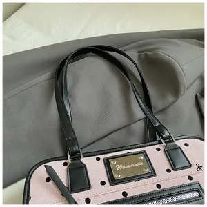 Gros plan d'un sac en toile rose à pois avec plaque de logo métallique et détails en cuir