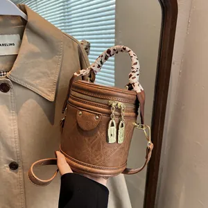 Close-up of brown barrel bag with gold padlock zip and scarf-wrapped handle detail