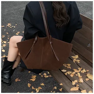 Detail of a large chocolate brown suede tote bag carried by a model in a fall park setting