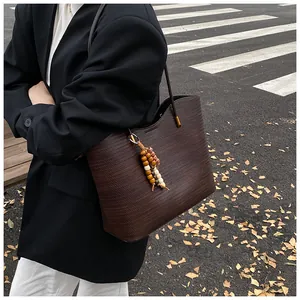 Detail of dark brown woven tote bag featuring a wooden bead charm and black leather handle