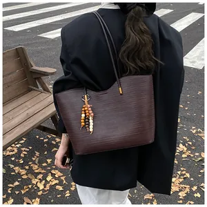 Detail of a dark brown woven tote bag with beaded tassel and thin leather straps