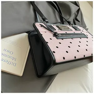 Détail du sac à main rose à pois avec garniture en cuir noir sur un trench-coat gris