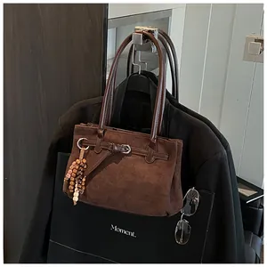 Detail der braunen Wildledertasche mit Lederriemen und Holzperlen-Anhänger am dunklen Blazer
