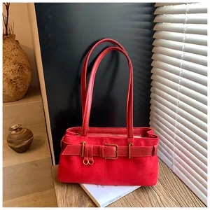 Gros plan du sac rouge en daim avec boucle en bronze vintage et bandoulière en cuir élégante