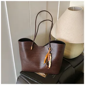 Detail of dark brown woven tote bag featuring a wooden bead charm and long handles