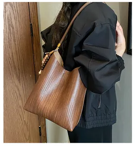 Sac à bandoulière marron texturé avec breloque en perles, porté par un mannequin en salle