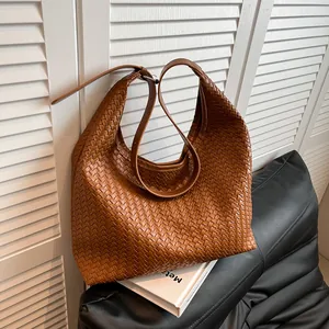 Detailed view of woven brown hobo bag texture and adjustable strap on leather sofa