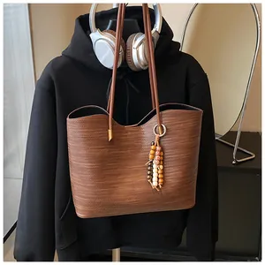 Detail of a brown woven tote bag featuring a decorative beaded tassel and long straps