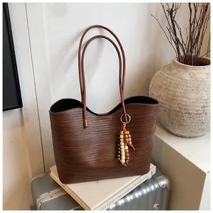 Detail of a large woven dark brown tote bag with beaded tassel and slim shoulder straps
