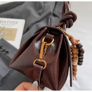 Detail of vintage brown leather bag with bronze hardware and wooden bead pendant