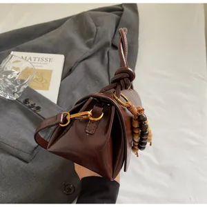 Close-up of a dark brown glossy leather handbag featuring a knotted handle and wooden bead charm