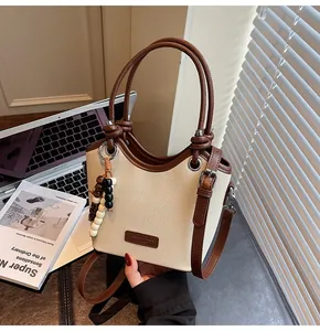 Détail du sac seau en toile avec garniture en cuir brun et pendentif perlé sous lumière douce