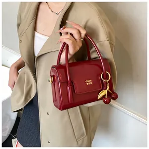 Detail of a shiny dark red patent leather handbag with a gold cherry charm and logo