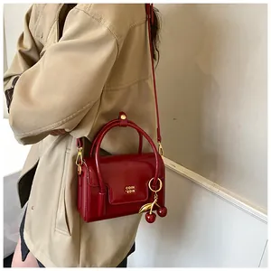 Macro detail of wine red glossy leather crossbody bag with cherry charm and gold logo