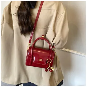Detail shot of a bright red patent leather handbag with a gold cherry charm on a model