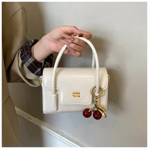 Chic cream white structured handbag with golden logo and a decorative cherry charm