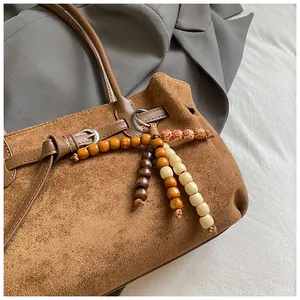 Detail der braunen Wildledertasche mit Metallschließe und dekorativem Holzperlen-Anhänger